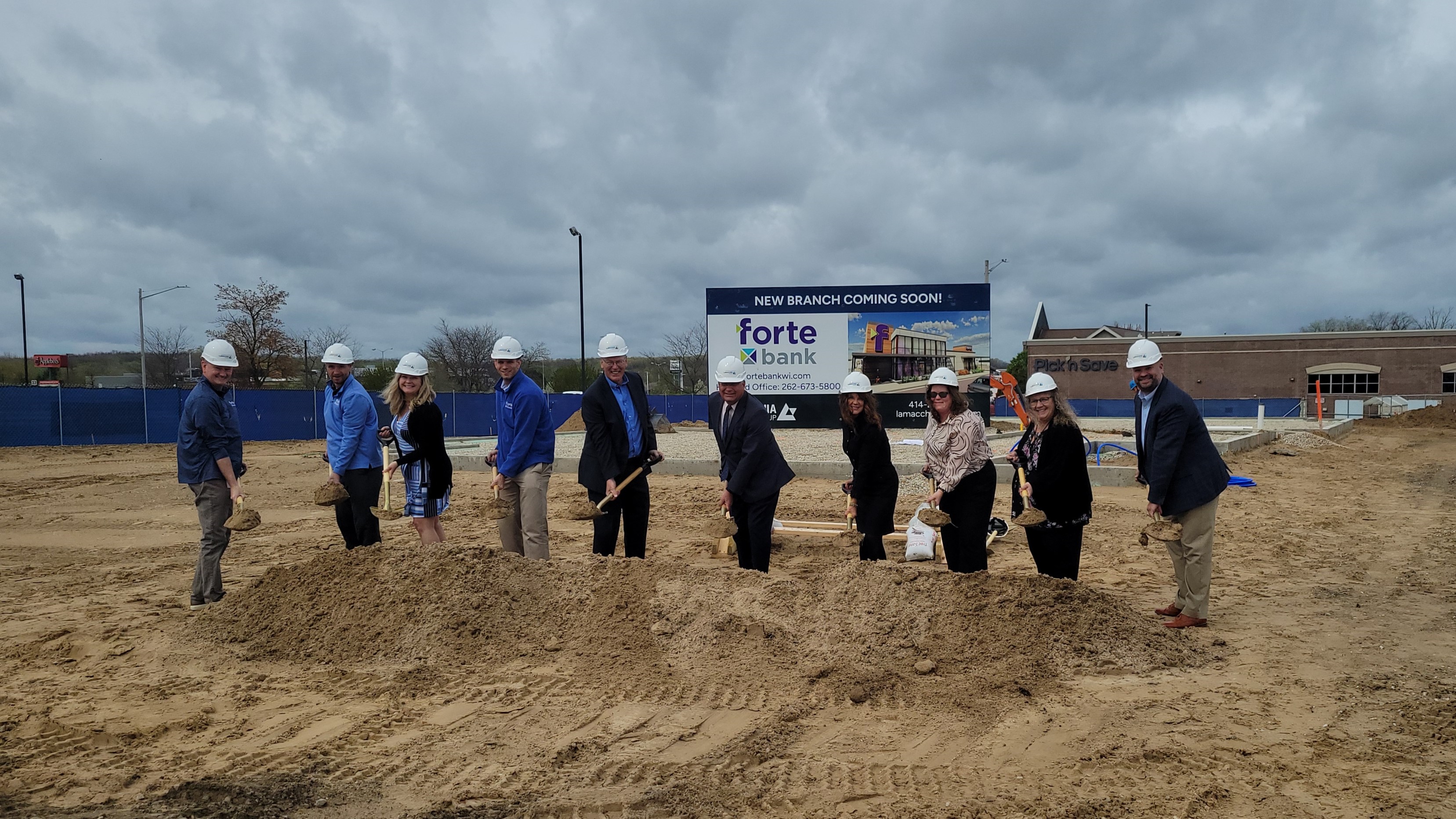 Ten employees of Forte Bank stand at the location of the new West Bend branch holding shovels with dirt at a groundbreaking ceremony.