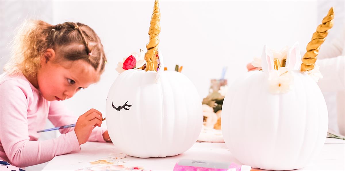 Girl painting a pumpkin like a unicorn.